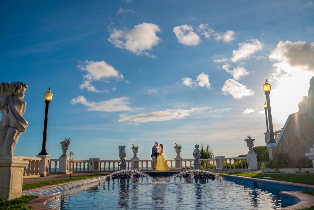Romantic sunset scene by an ornate pool with statues and torches along a waterfront terrace.