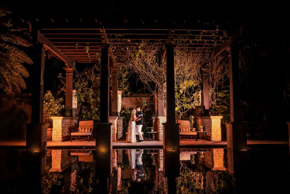 A romantic evening reflection of a couple silhouetted under a pergola with decorative lighting.