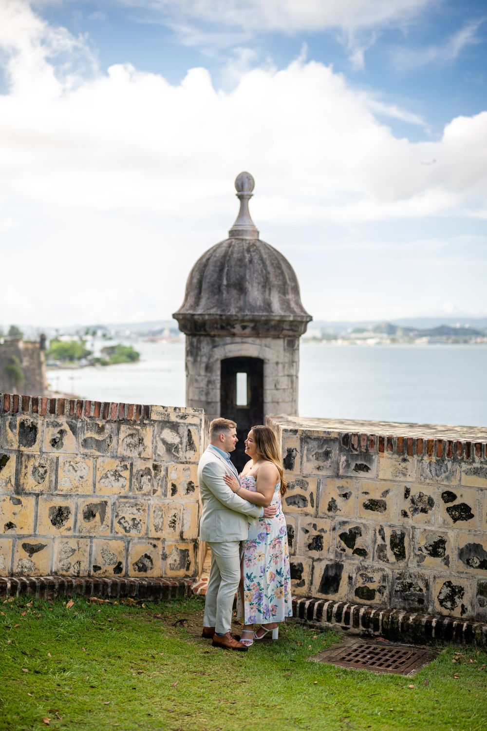 A couple embraces near a historic stone watchtower overlooking a coastal vista.