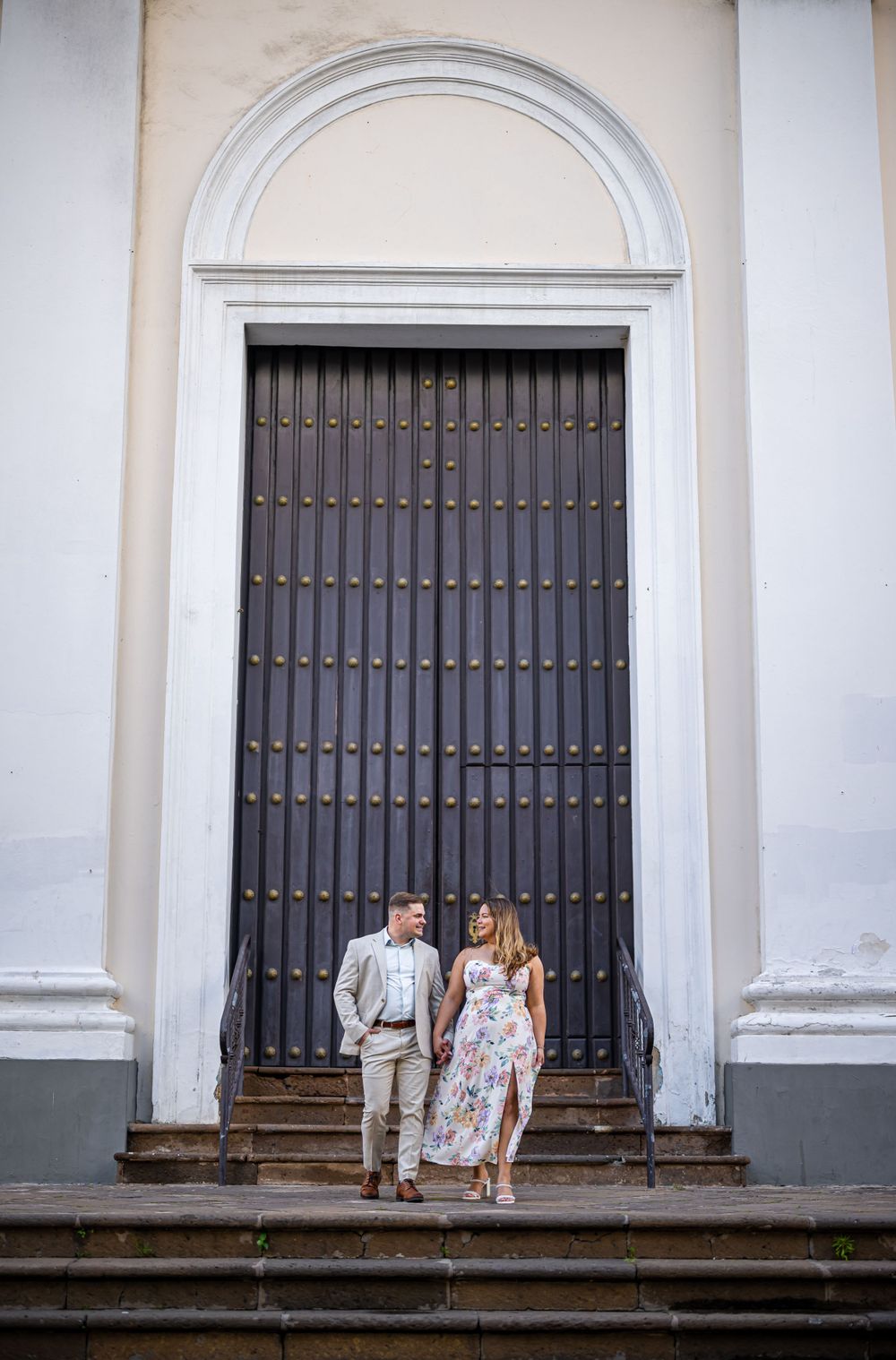 A couple stands at the base of a grand arched doorway with ornate metal gates.
