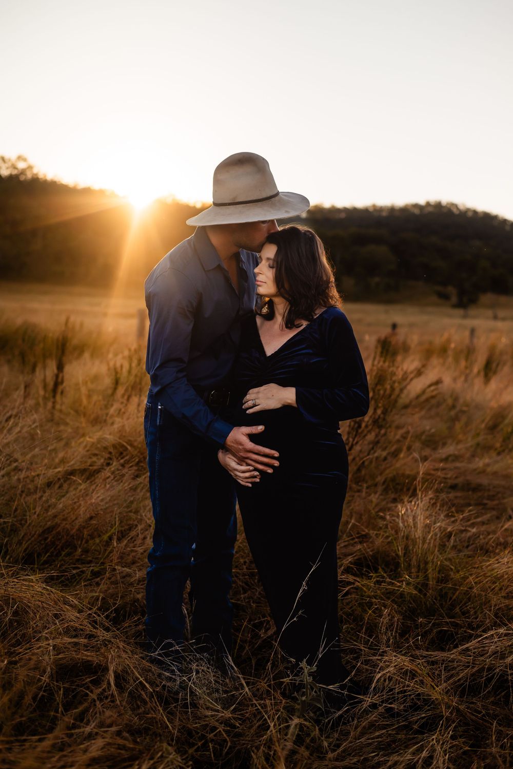 A tender moment between a couple in a golden field at sunset.