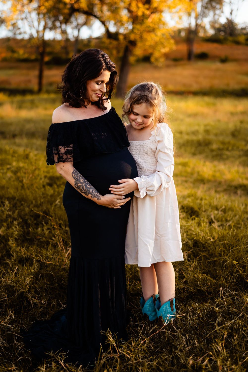 A maternity moment shared between mother and child in an autumn field at sunset.