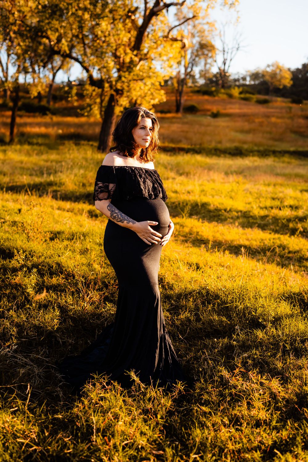 A maternity portrait in a black dress against golden autumn foliage.