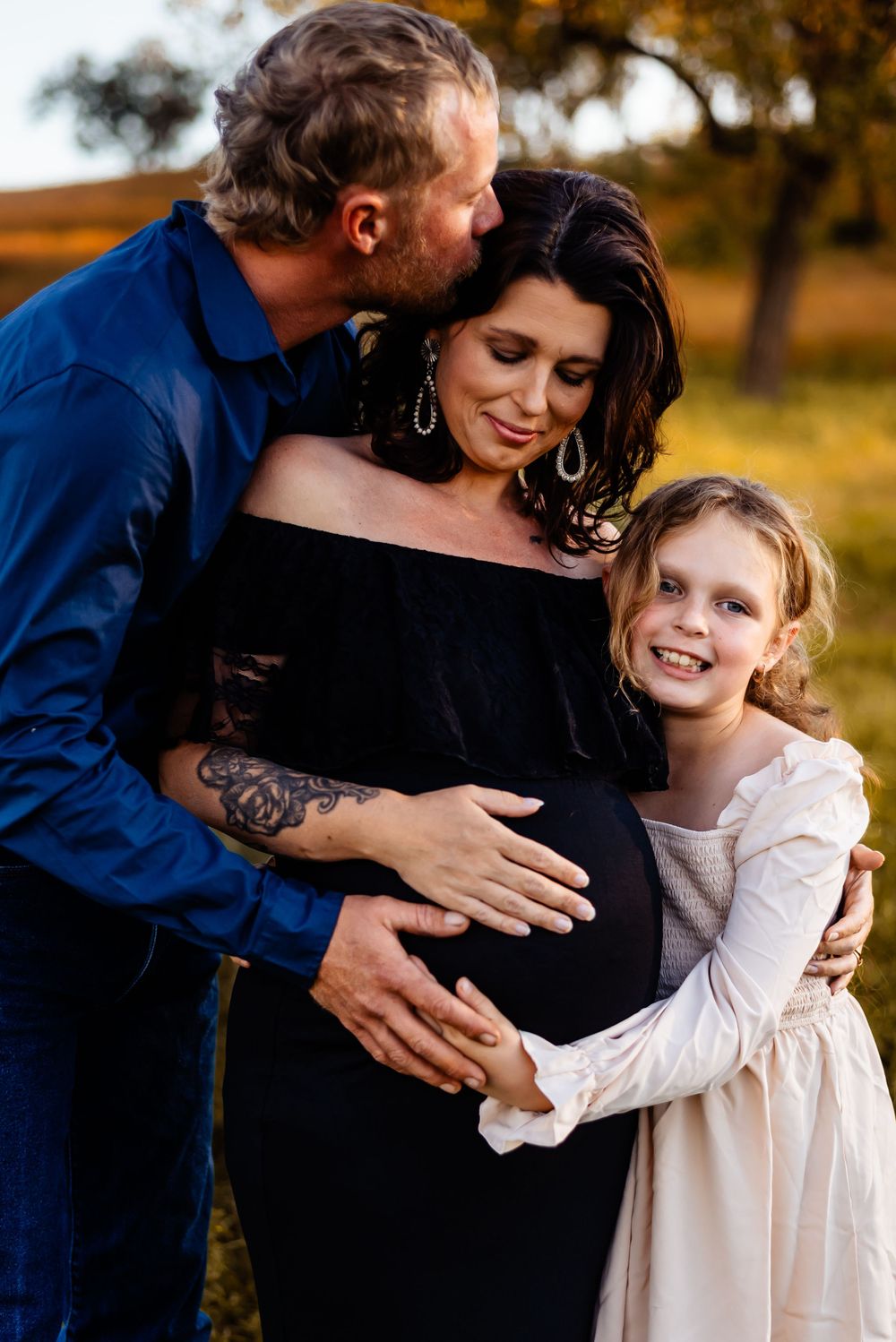 Family shares intimate moment during sunset maternity photoshoot in field.