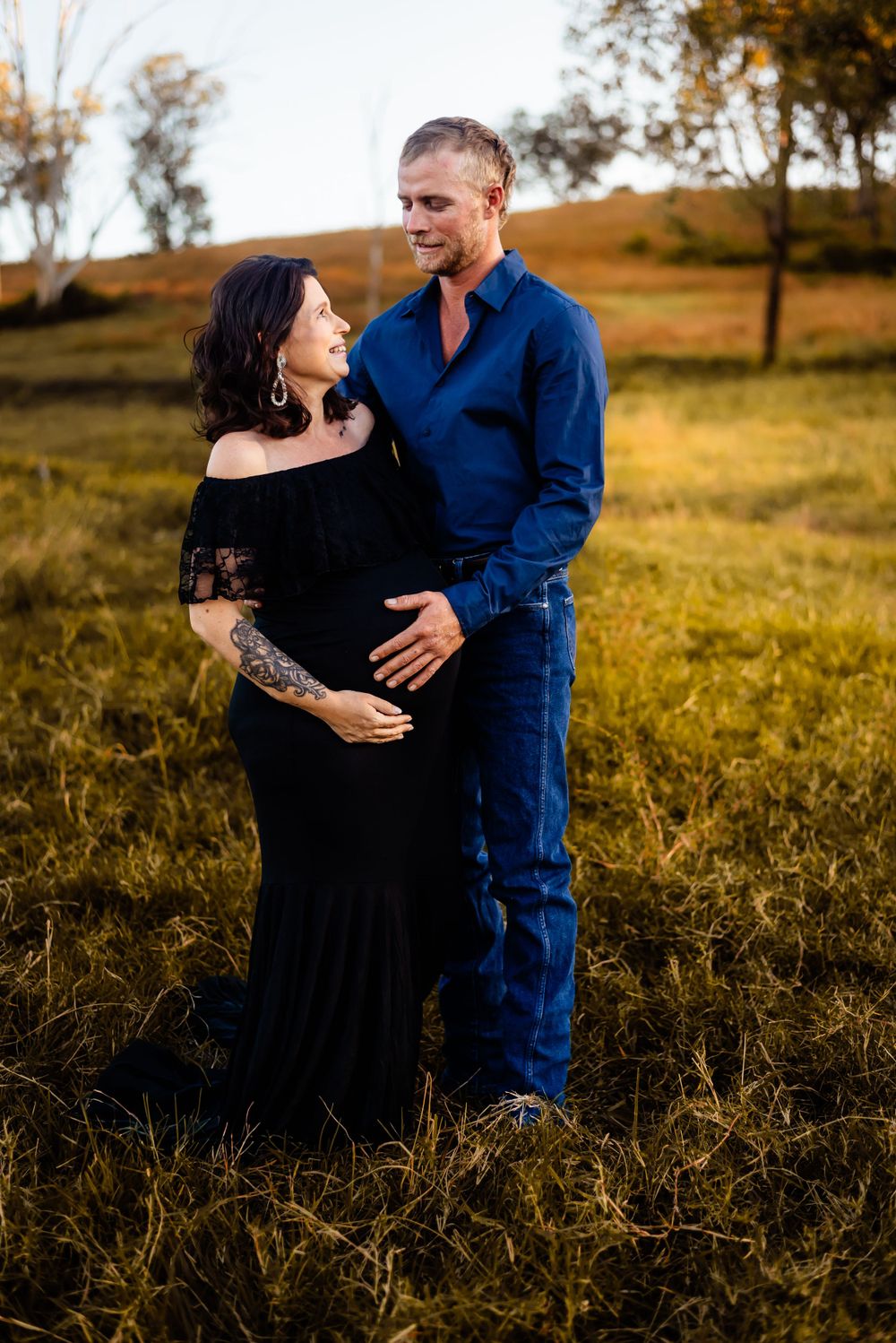 Couple shares tender moment in golden field during maternity photoshoot.