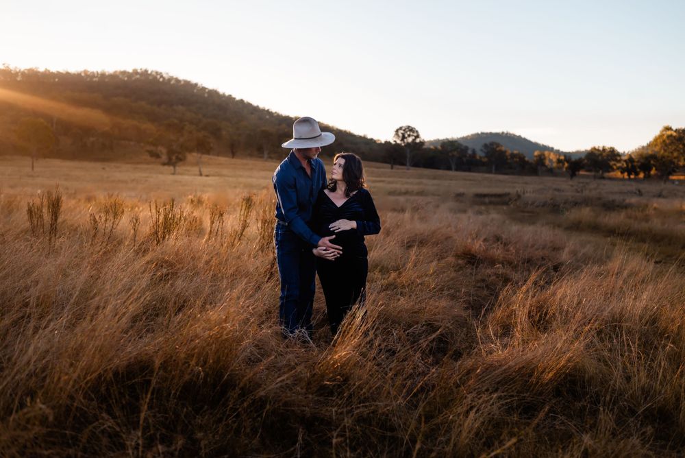 Couple shares intimate moment in sunlit field during golden hour.