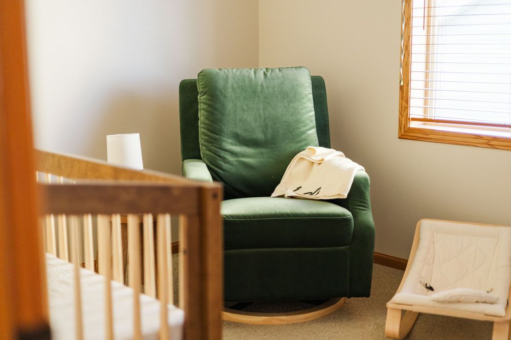 Modern nursery interior with green armchair and wooden crib.