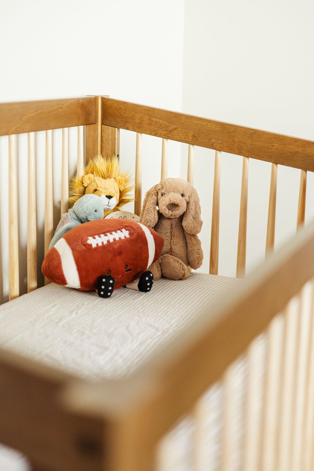 Wooden crib with plush toys including football and teddy bears.