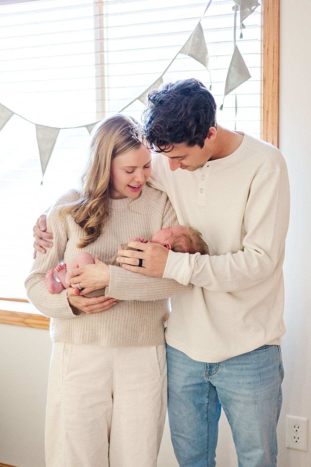 Family gathering around newborn baby in cozy neutral-toned room with bunting decorations.