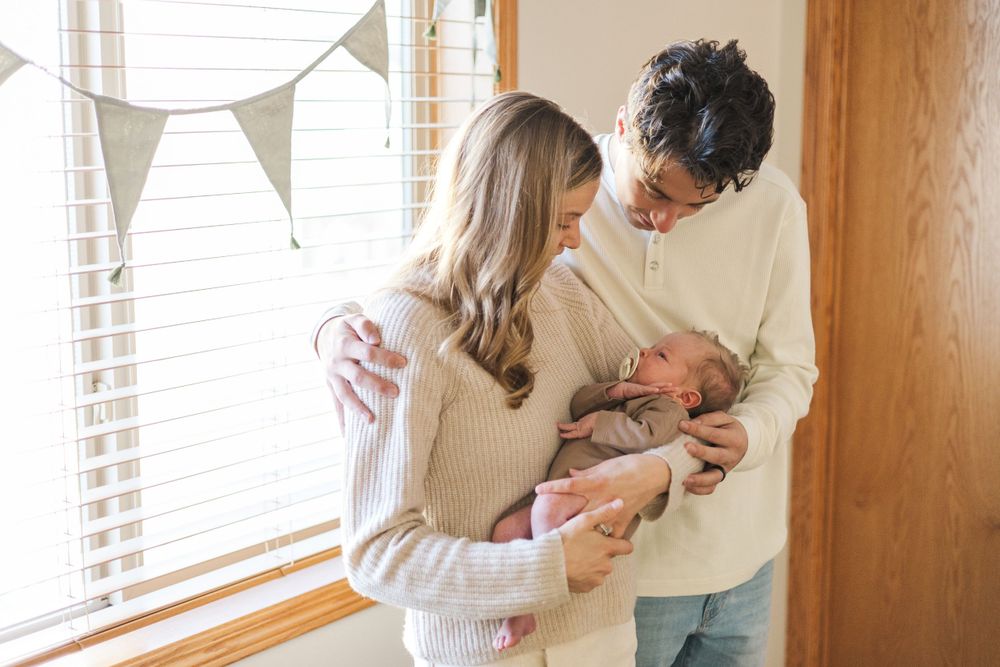 Parents sharing loving moments with their infant in a sunlit room with white bunting.
