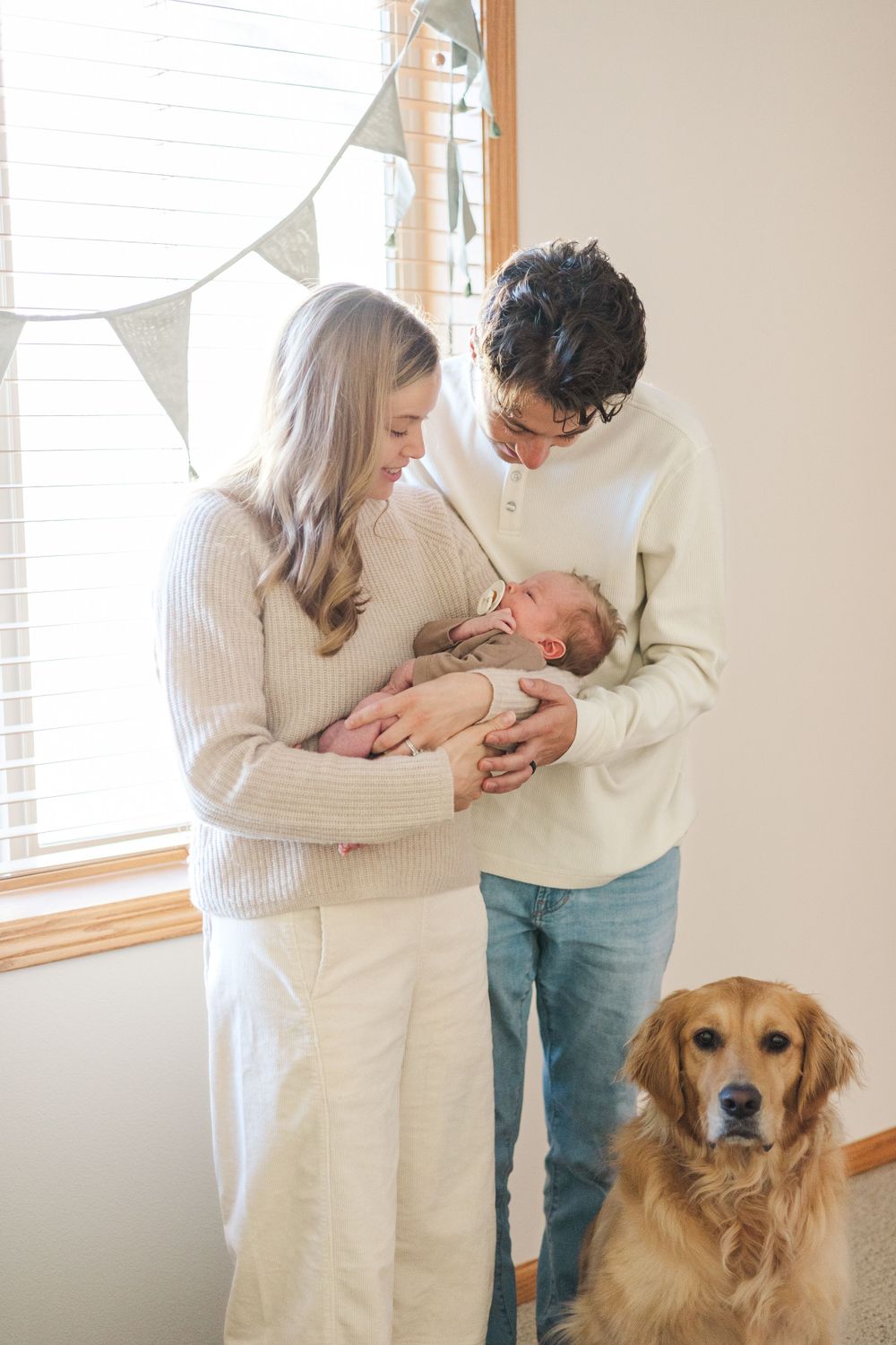 A family moment with their newborn baby while their golden retriever watches nearby.