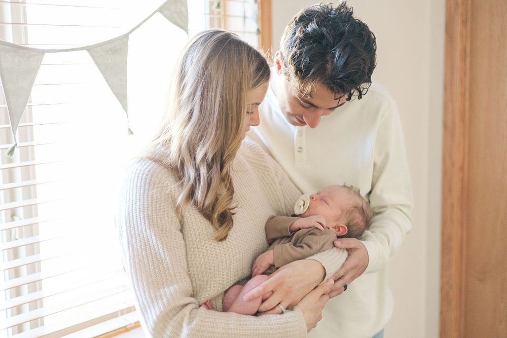 Parents in matching light colored sweaters gazing lovingly at their baby.
