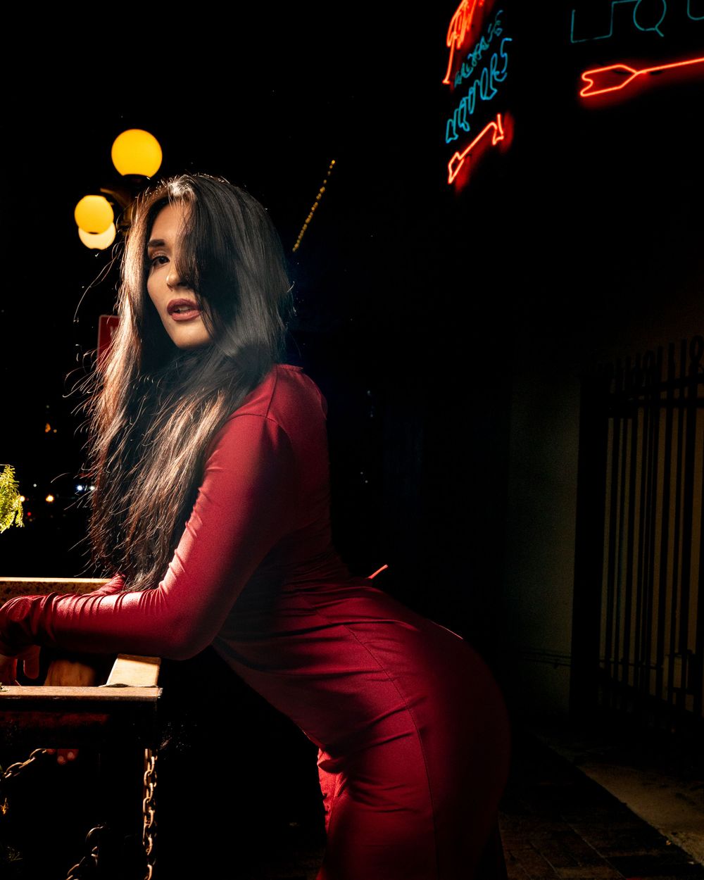 Moody nighttime fashion portrait in red dress against neon lights.