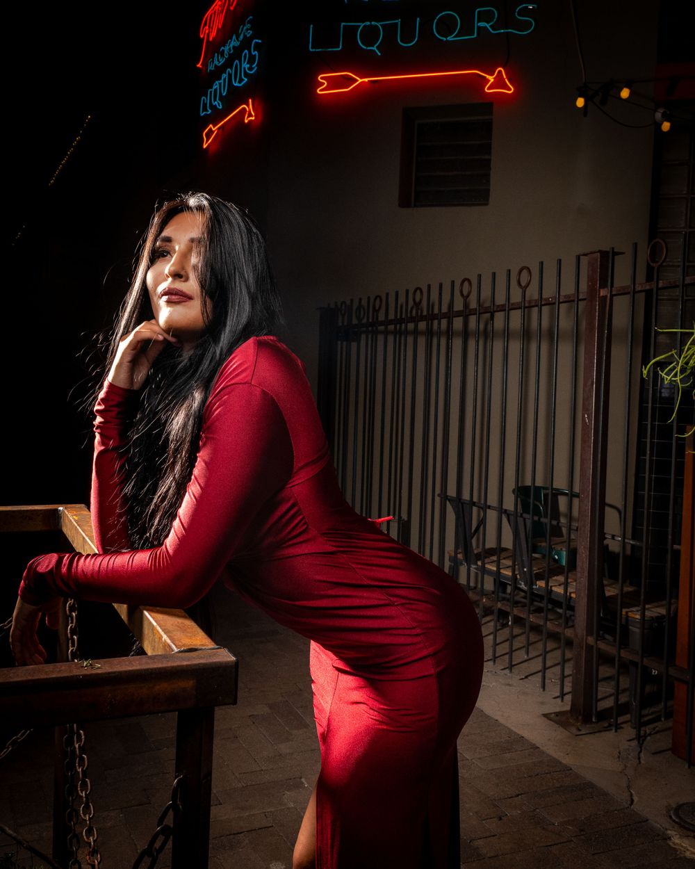 Dramatic pose in red dress against neon liquor store sign at night.