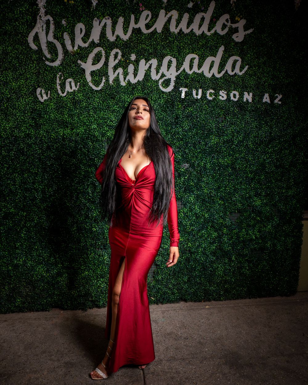 A stunning long red dress with thigh slit is showcased against a decorative green wall backdrop.