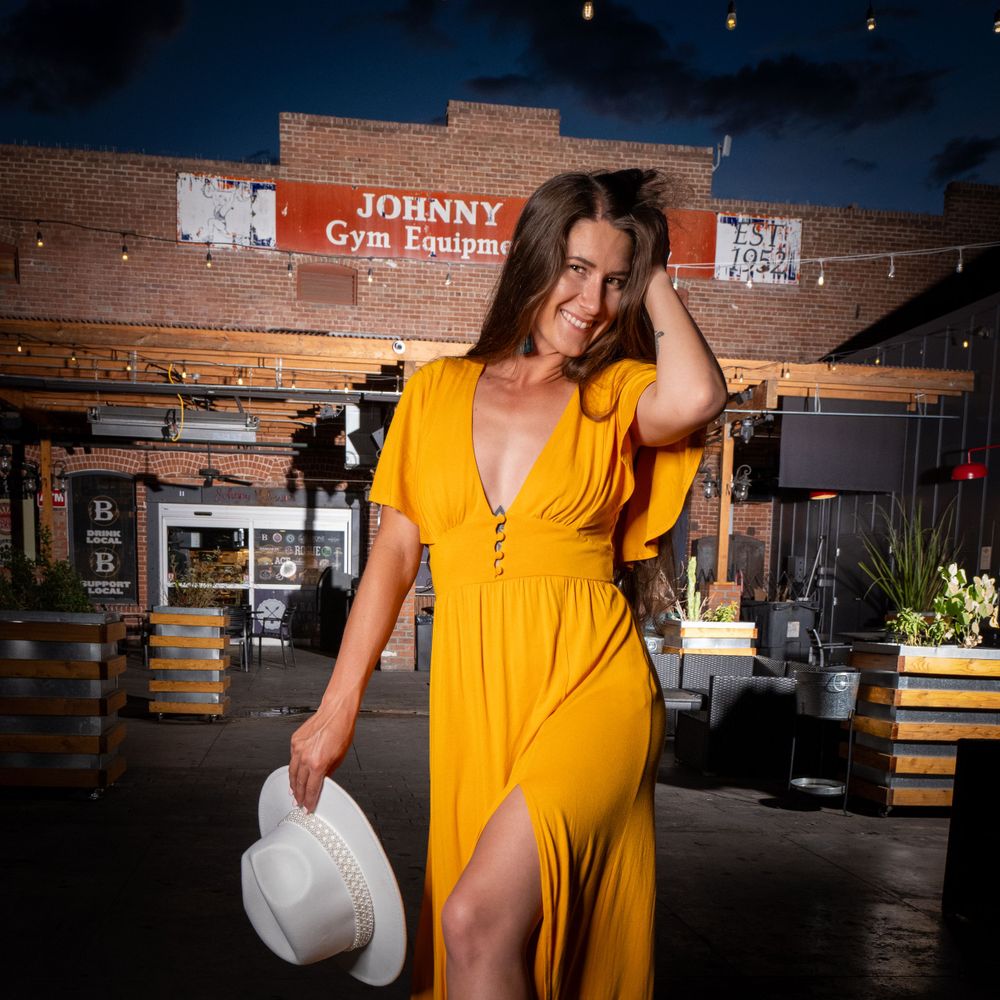 Yellow sundress and white hat photographed at dusk against rustic brick wall setting.