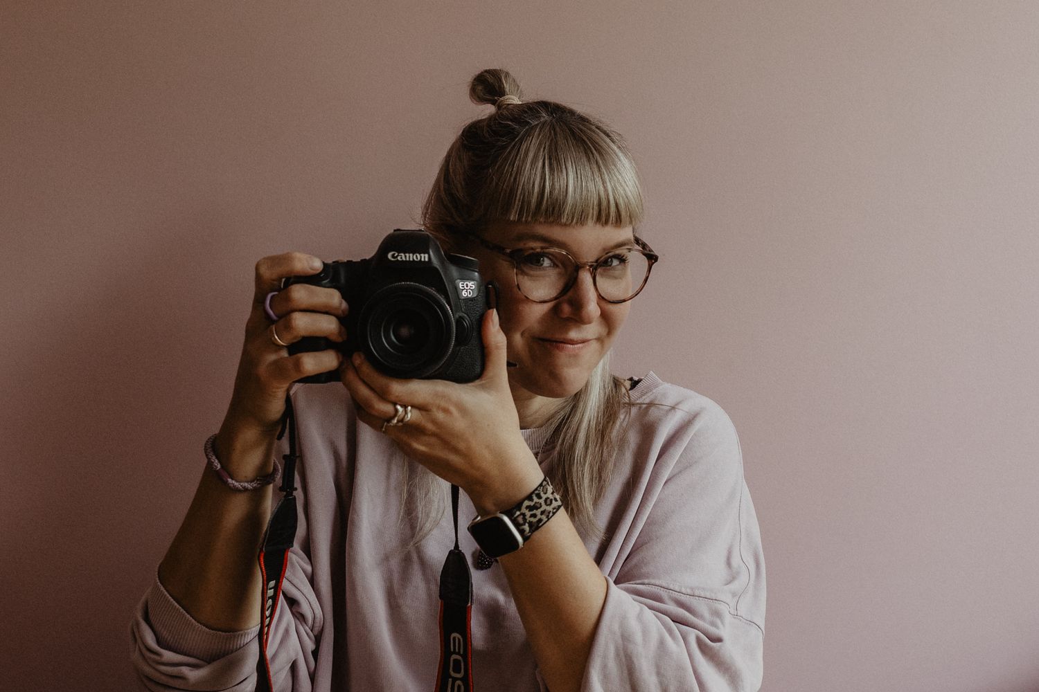 Ein gemütlicher Moment der Fotografin mit einer Tasse, sitzend vor einer rosa Wand.