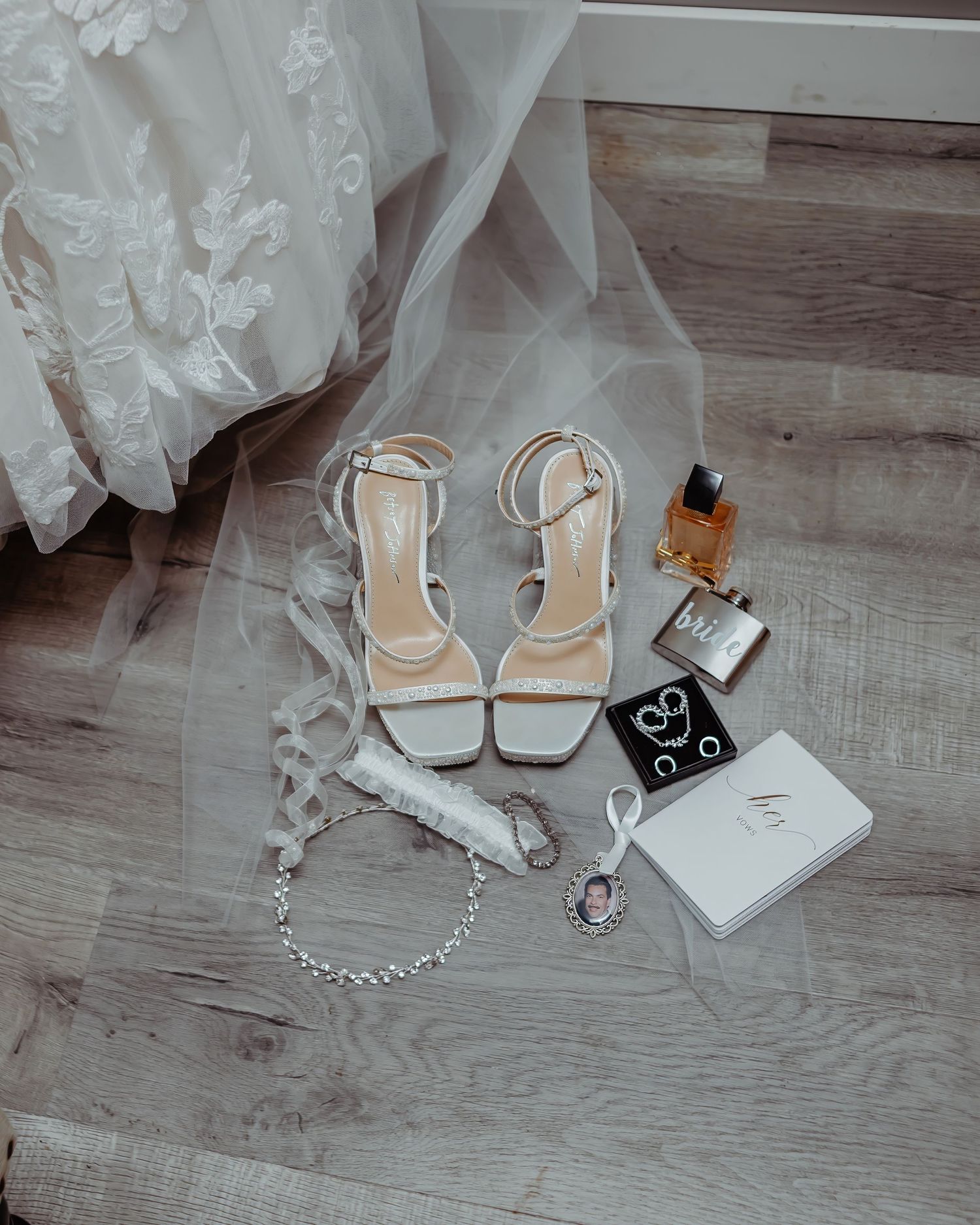Wedding accessories including white heels, veil, and jewelry arranged on wooden flooring.