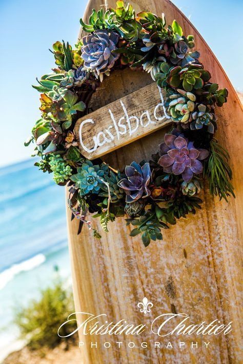 A rustic wooden sign with 'Gailsbache' text decorated by a wreath of colorful succulents against an ocean background.