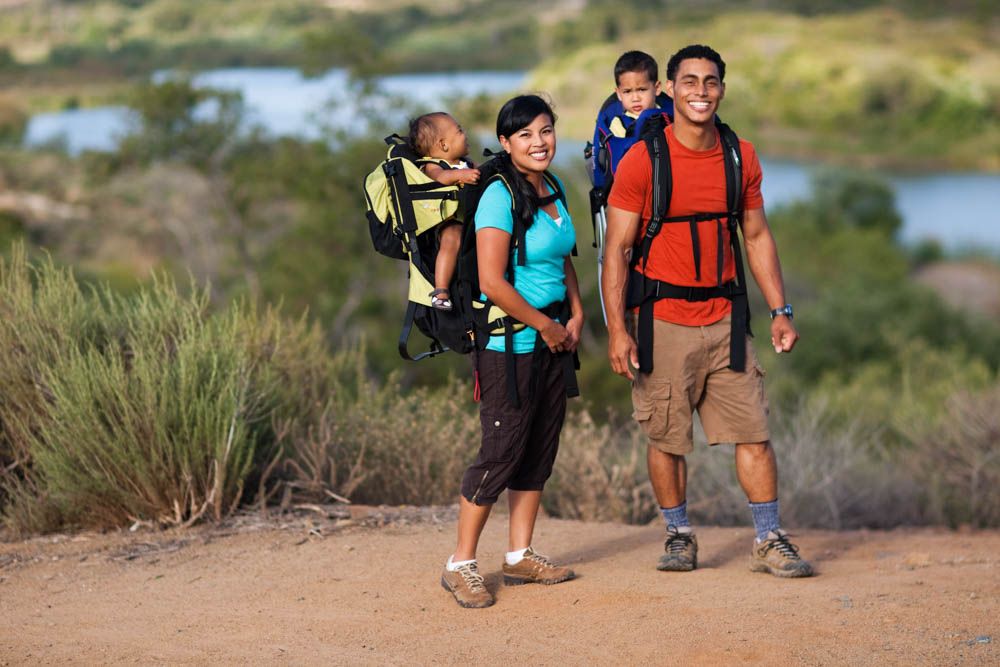 Hikers with backpacks traverse a scenic desert trail through rugged terrain at sunset.