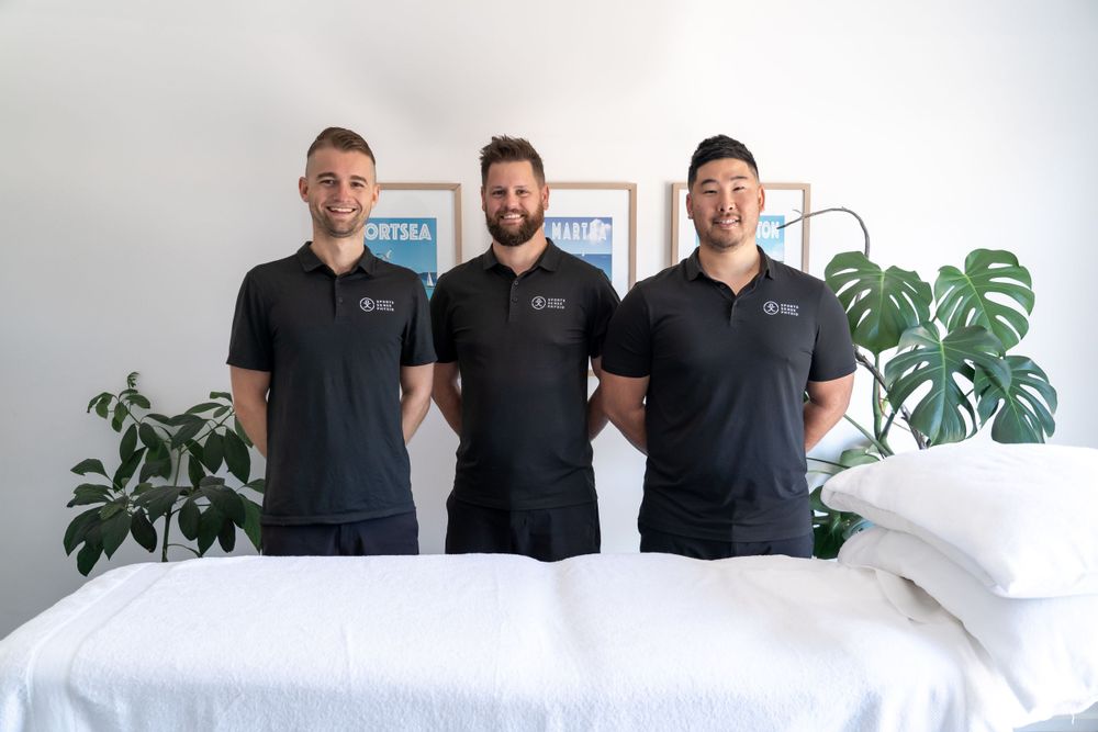 Three physiotherapy professionals in black uniforms standing together in clinic.