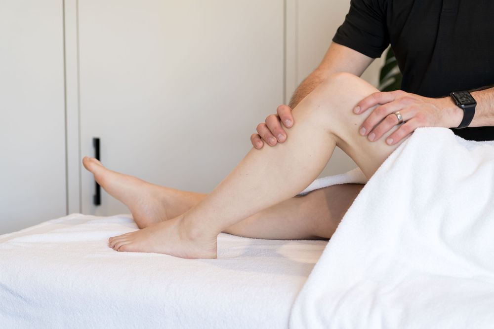 Professional physiotherapist performing therapeutic leg massage on treatment table.