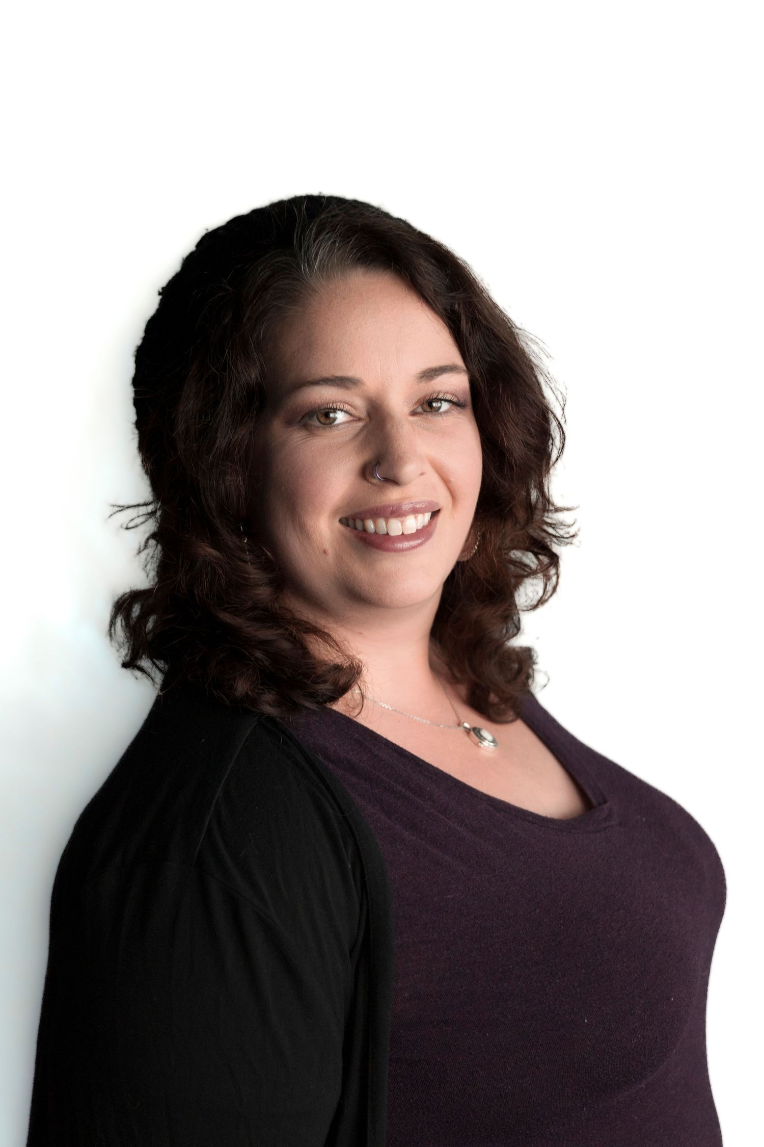 Professional headshot of a person in black and purple outfit with curly hair against white background.