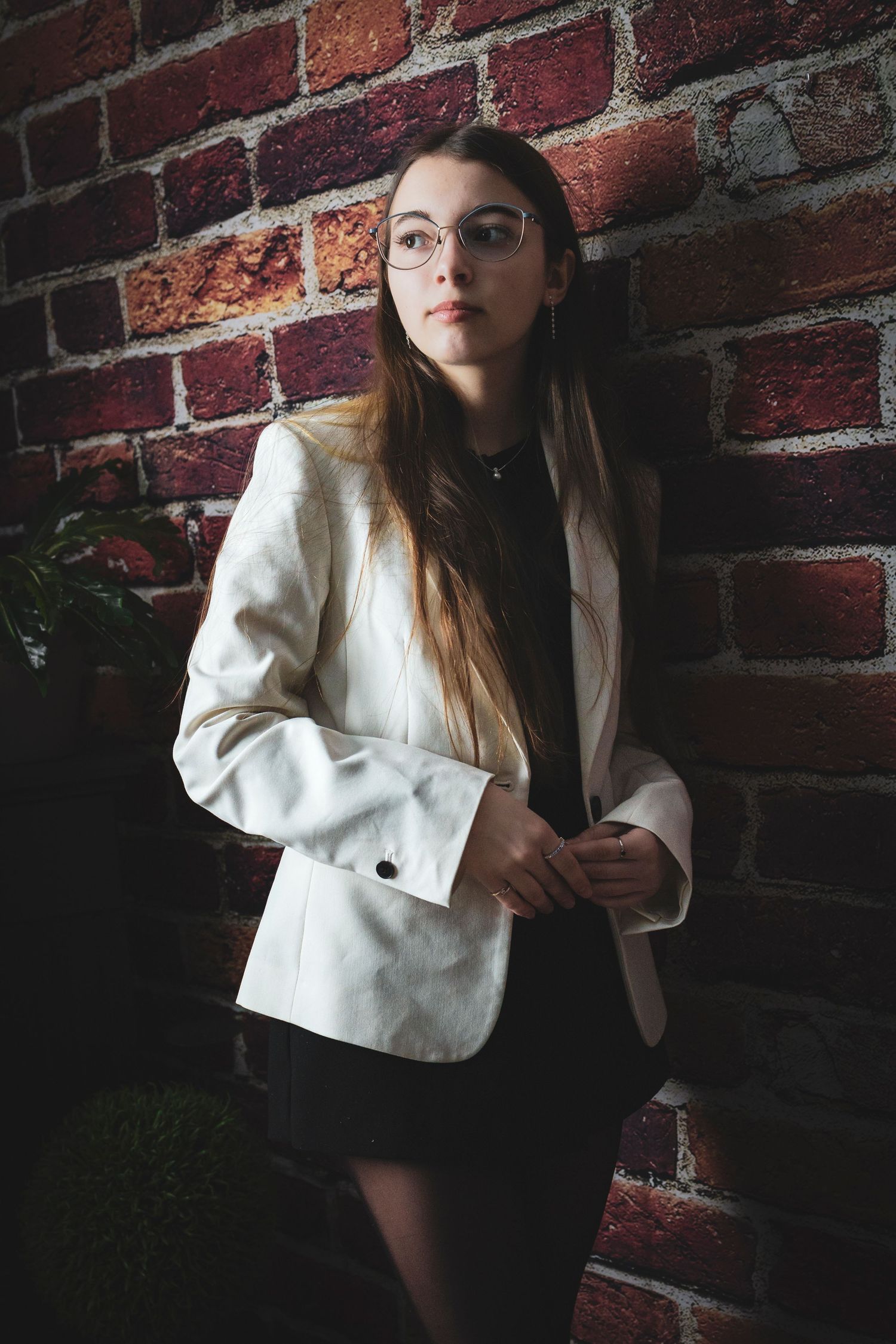 Artistic portraits against red brick wall wearing white blazer and black dress.
