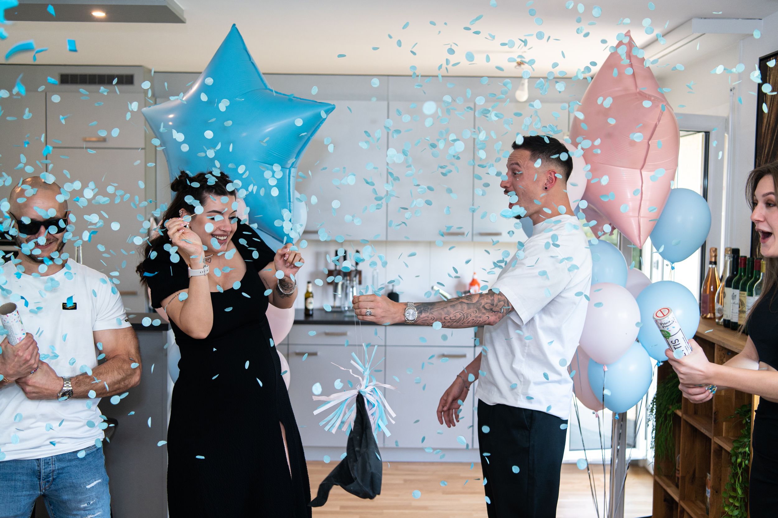 Couple celebrating gender reveal with blue star balloons and confetti in bright indoor setting.
