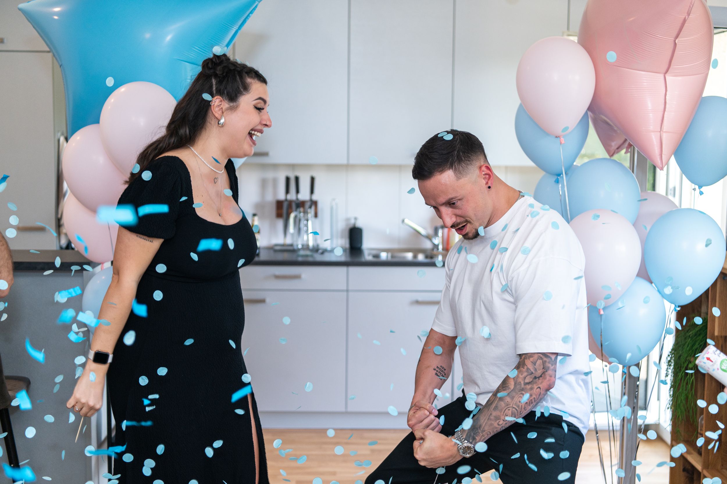 Gender reveal celebration with blue and pink balloons as couple reacts to the surprise.