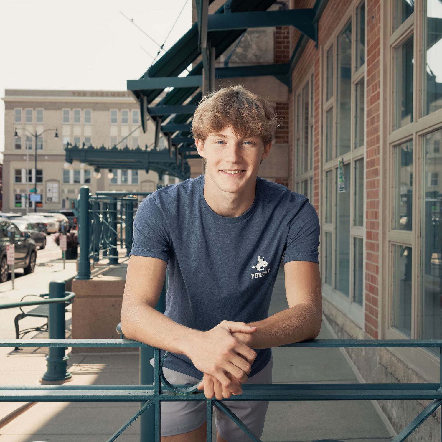 Person in blue t-shirt leaning on railing outside brick building with architectural details visible.