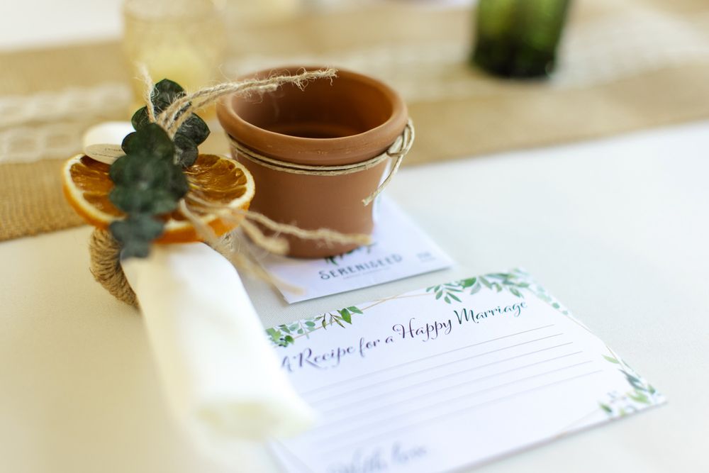 Recipe card with green leaves design sits beside a small terracotta planter and dried citrus slice on white table.