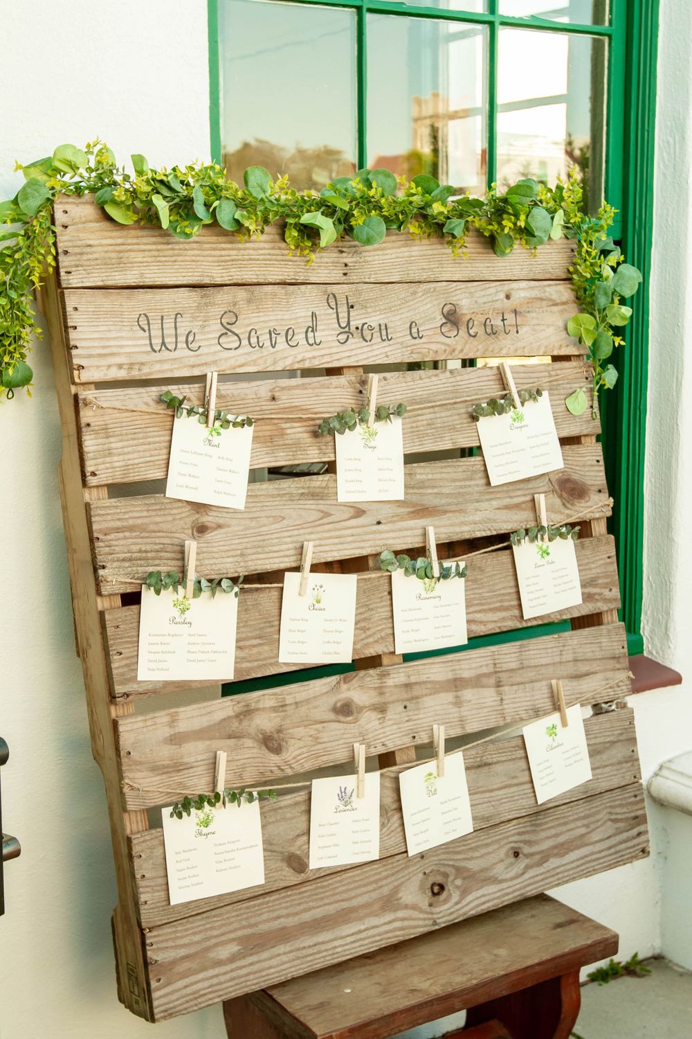 Rustic wooden pallet wedding seating chart decorated with greenery and clothespinned escort cards hanging on twine.
