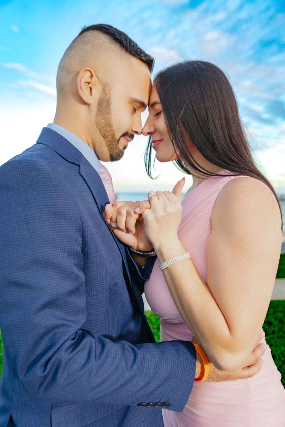 Romantic couple in formal attire share an intimate moment outdoors against a blue sky background.