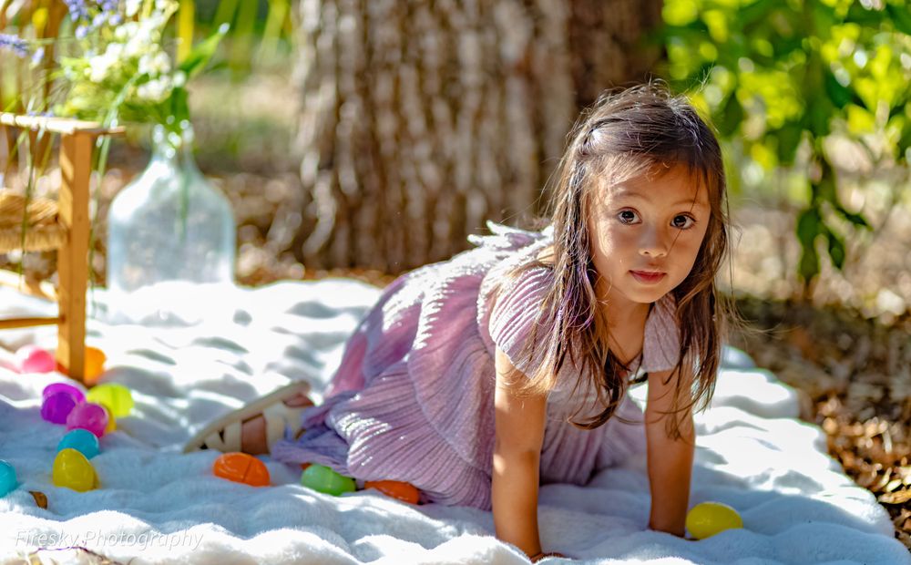 A child plays with colorful toys while crawling on white sand in a garden setting.