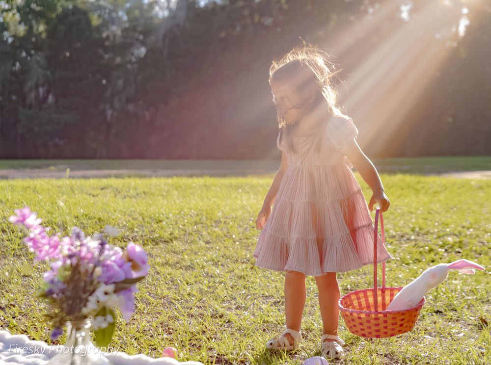 Young child in pink dress playing in sunlit garden with flower basket.