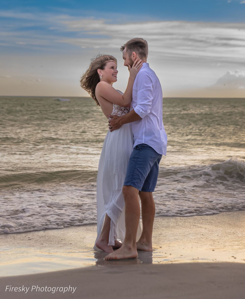 Couple in white and blue outfits dancing on beach during golden hour.