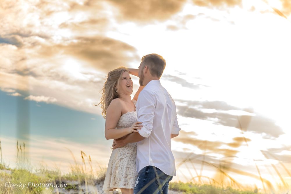Couple embracing in field during dramatic sunset with golden light streaming through clouds.