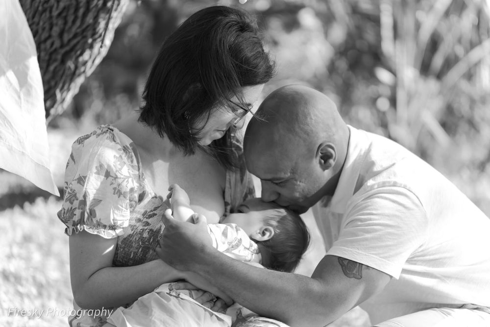 A tender black and white family moment as parents cuddle with their newborn baby outdoors.