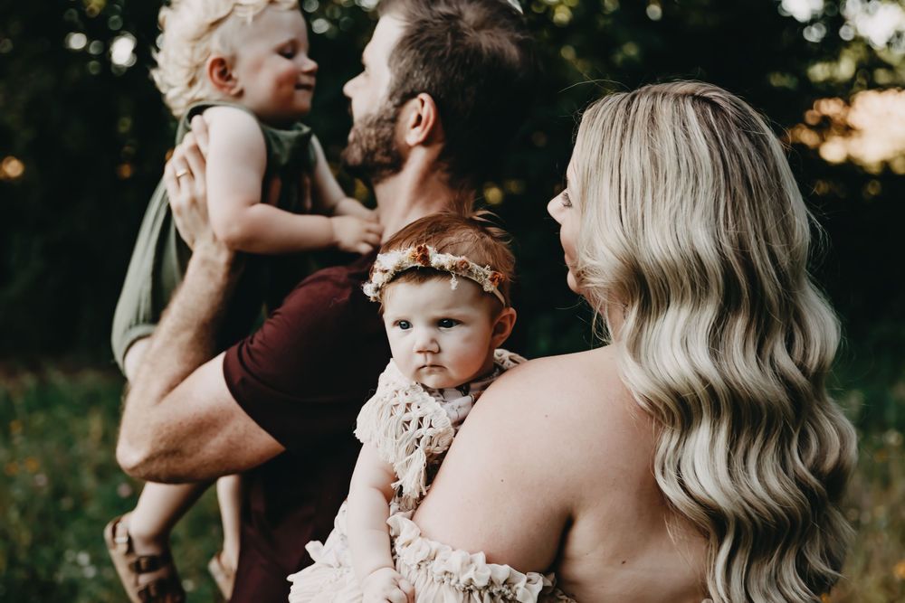 An intimate family portrait backlit by golden sunlight in a natural outdoor setting.