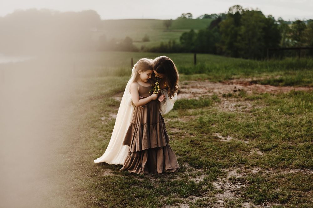 Two small children play together in a rustic outdoor setting wearing flowing dresses on a misty afternoon.