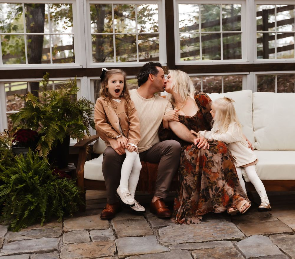 Family shares a playful moment together while sitting on an outdoor patio couch surrounded by potted plants.