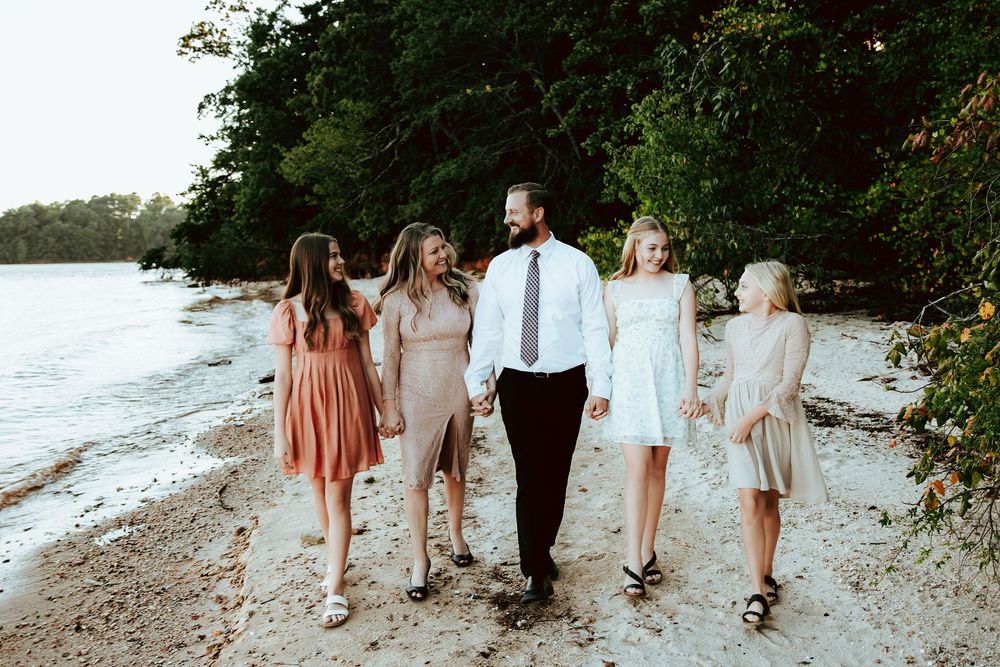 Group walking together on a beach shore wearing pastel dresses and formal attire at sunset.
