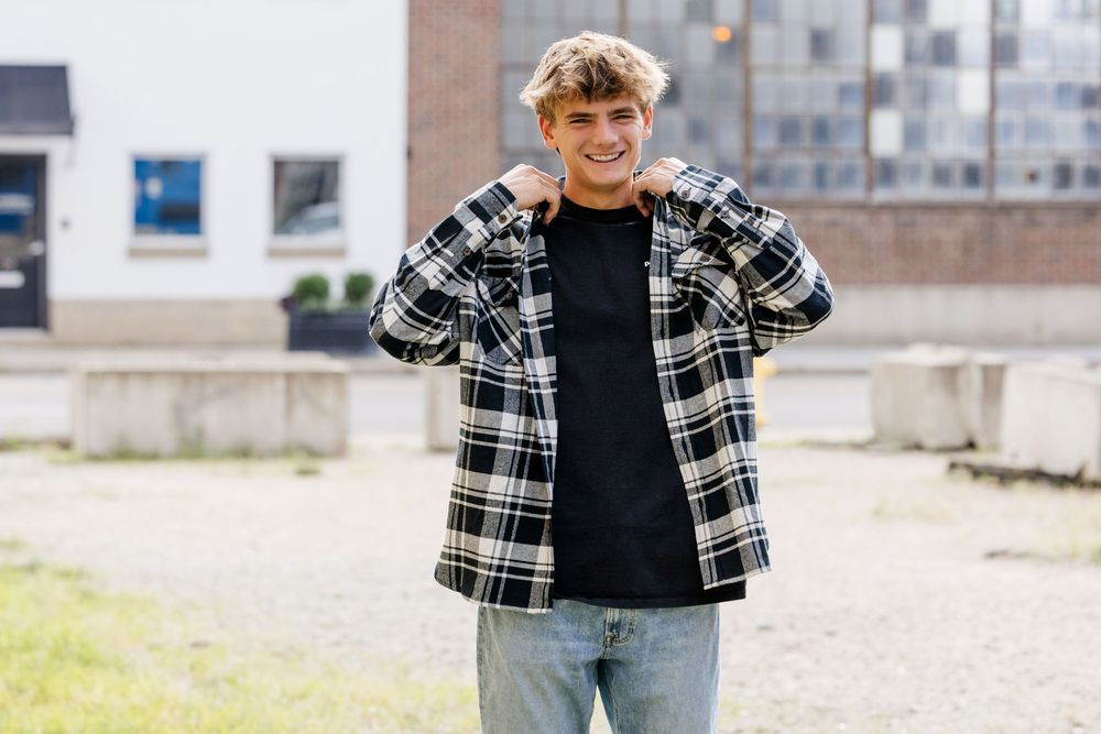A person wearing a black and white plaid flannel shirt and jeans stands in a casual pose outdoors.