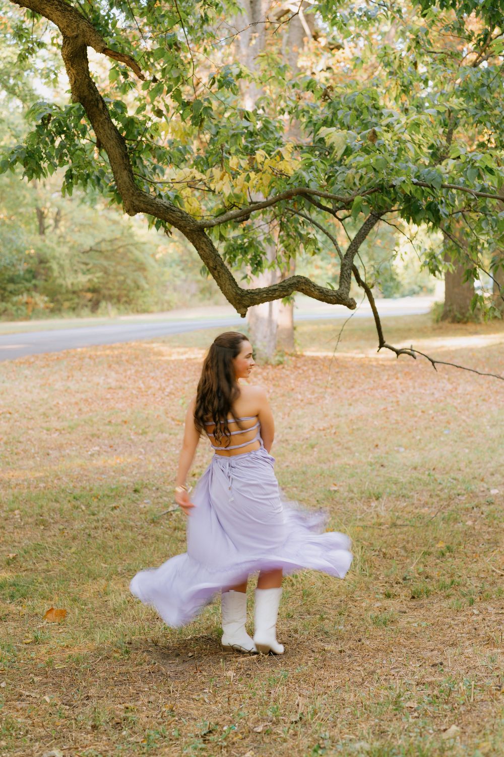 A person in a flowing lavender dress spins gracefully under a tree in a dreamy autumn setting.