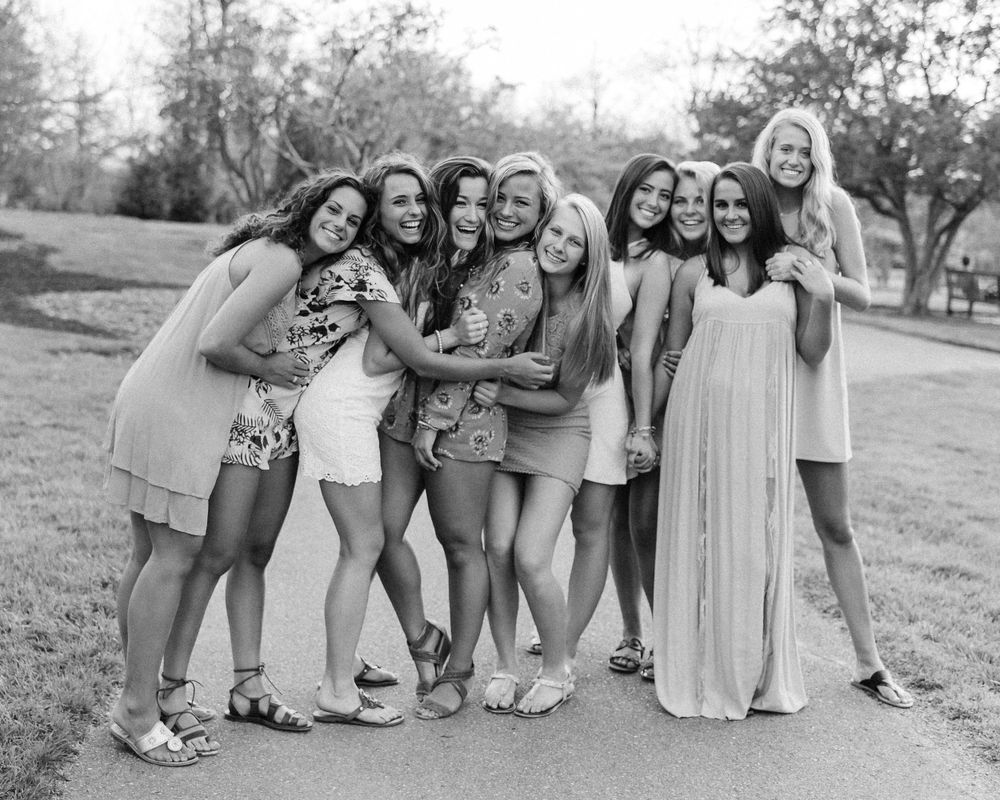 A group of friends in light summer dresses pose together outdoors in a black and white photo.