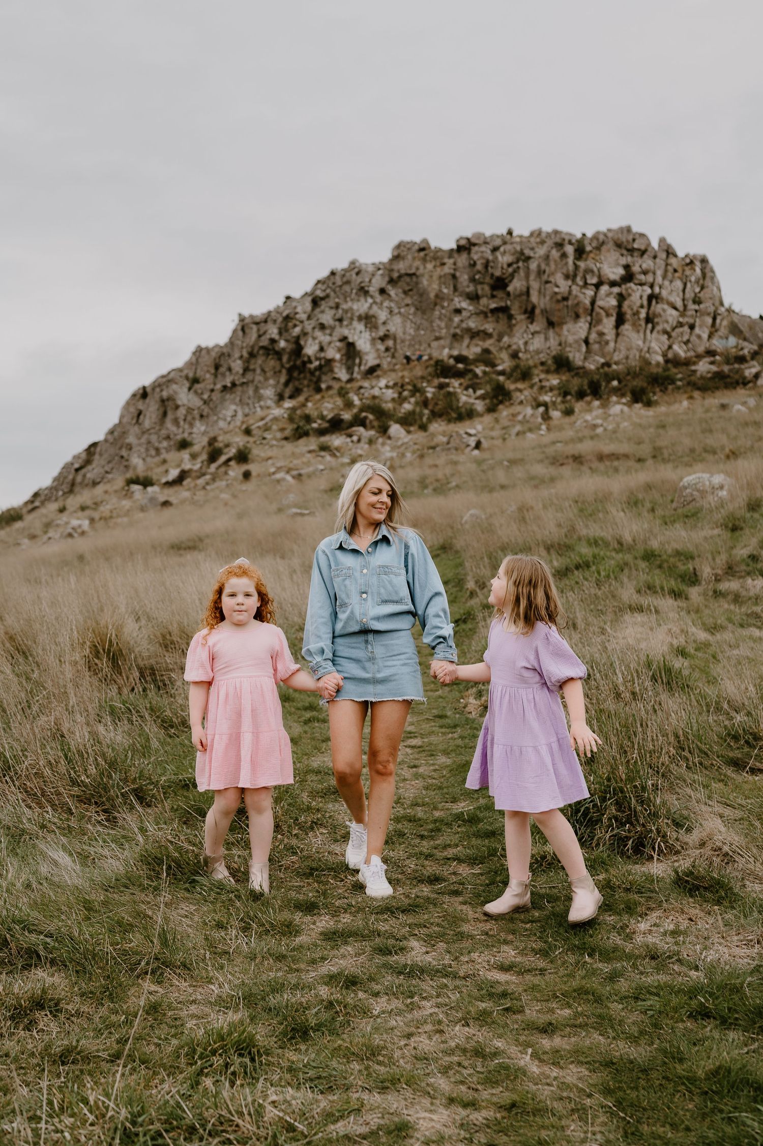 Three figures walking along a trail with a dramatic rocky outcrop in the background.