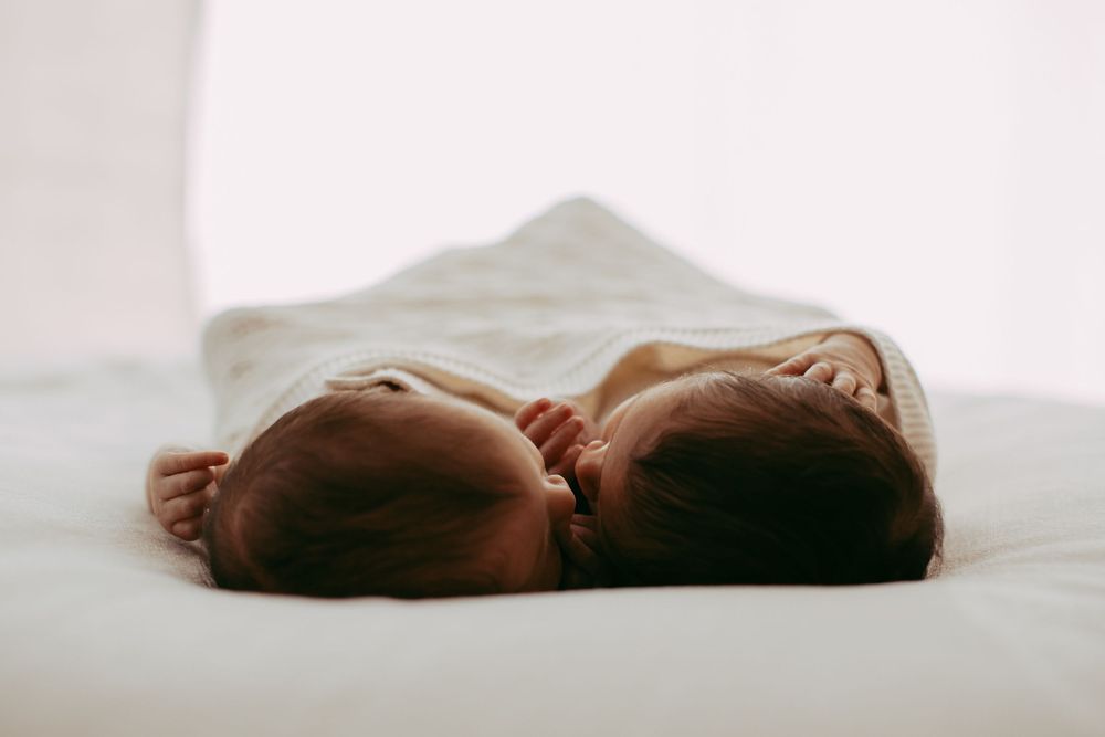 Close-up view of a sleeping baby swaddled in white fabric against a light background.