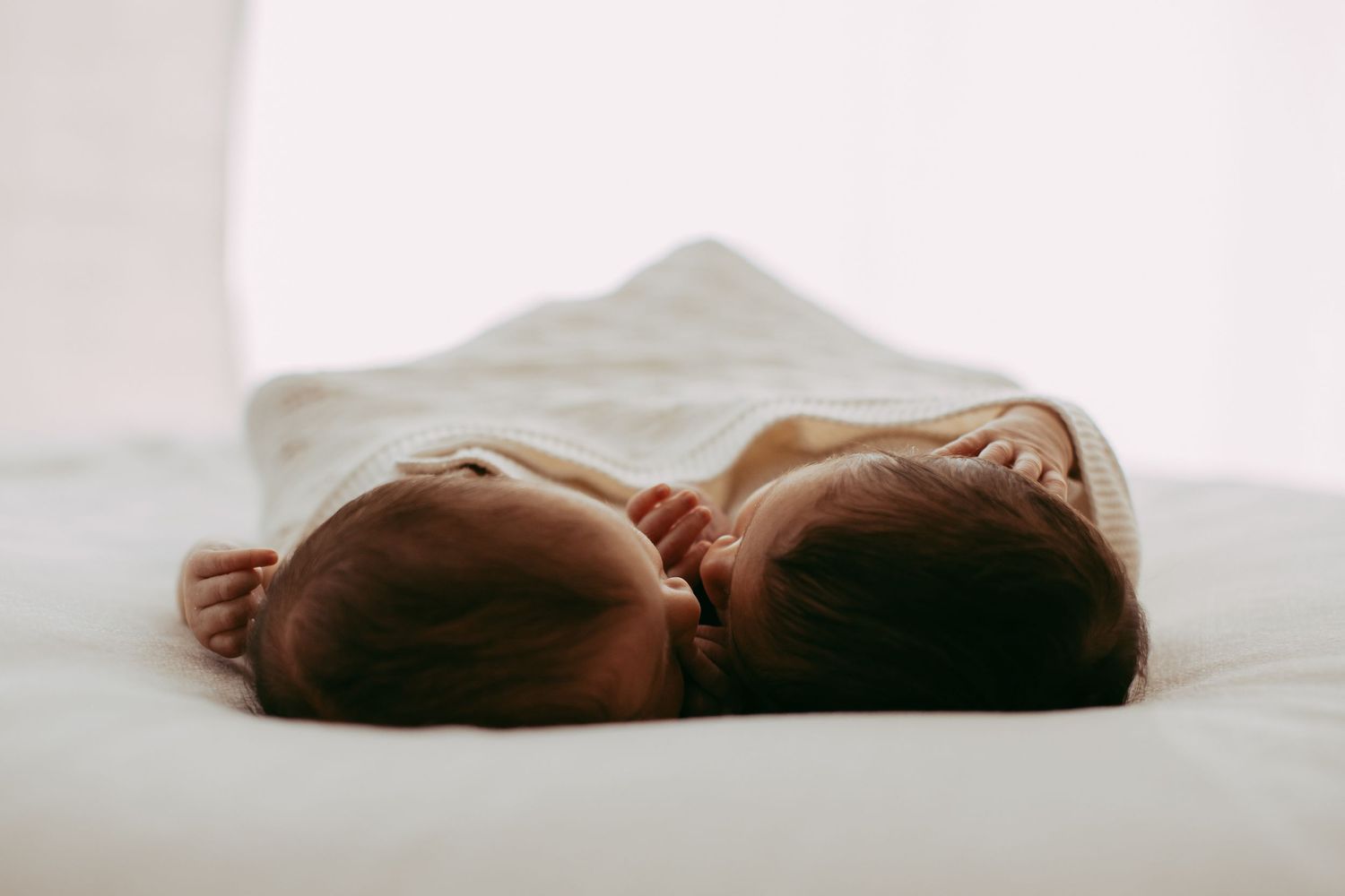 Close-up view of a sleeping baby swaddled in white fabric against a light background.
