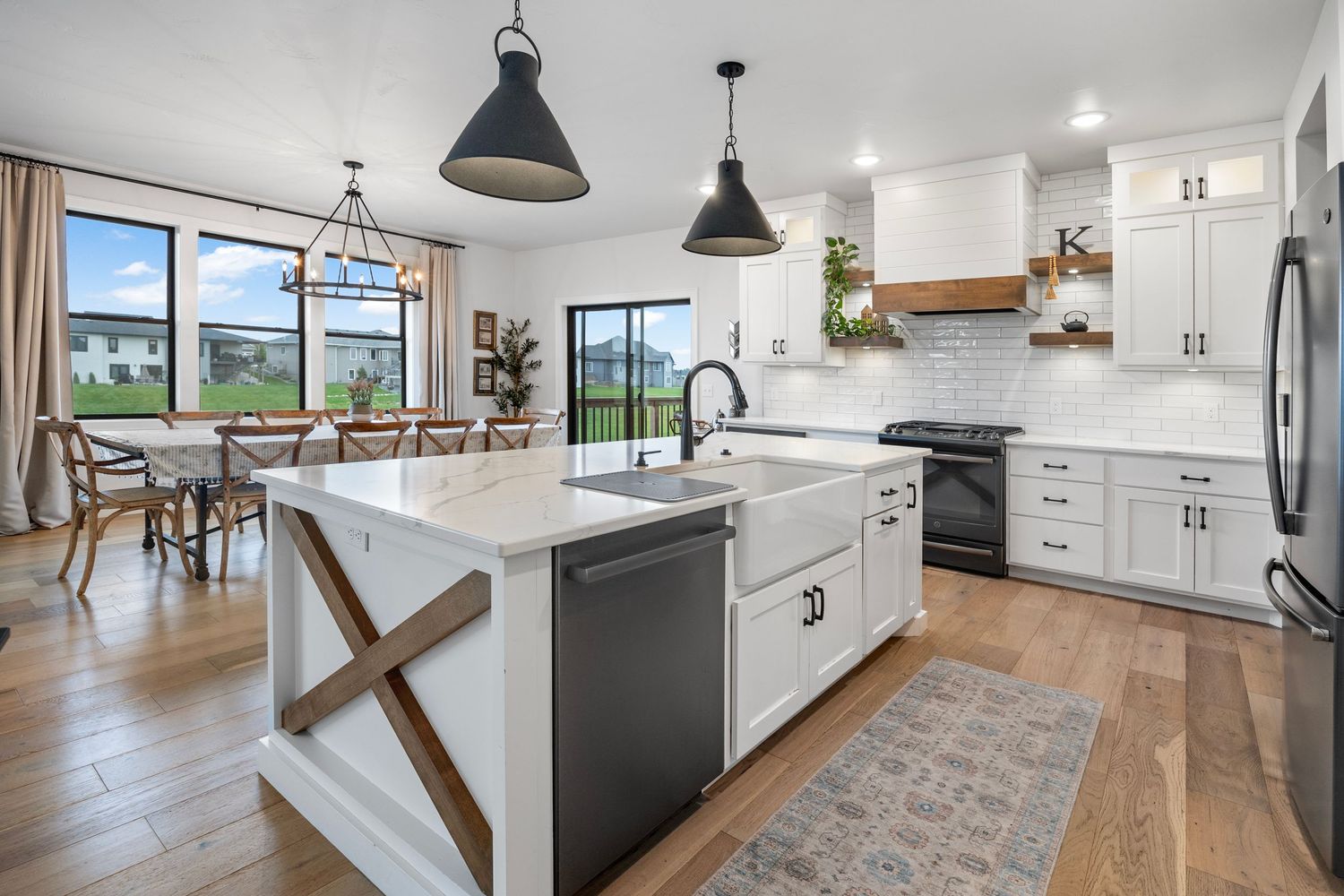 Spacious white kitchen with large island, pendant lights, and hardwood floors.